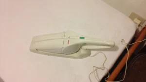 Aspirateur à main sans fil blanc posé sur un lit, à côté de son socle de recharge